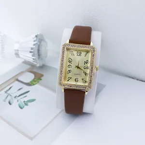 Close-up van een vierkant strass-horloge met gouden kast en een bruine lederen horlogeband.