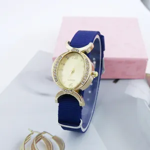 Detalle de reloj de cuarzo ovalado con caja dorada de diamantes y correa de nailon azul.