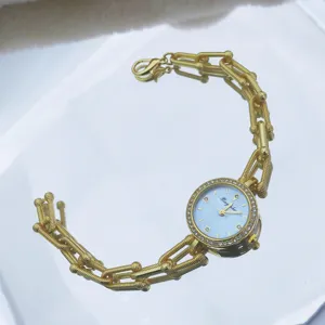 Nahaufnahme einer goldenen Quarzuhr mit Strasslünette, blauem Zifferblatt und Kette.