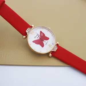 Primer plano detalle de reloj de mujer de cuarzo con correa de cuero rojo y esfera de mariposa.