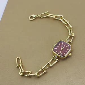 Detailaufnahme einer vergoldeten Quarzuhr mit rotem quadratischen Zifferblatt und Gliederarmband.