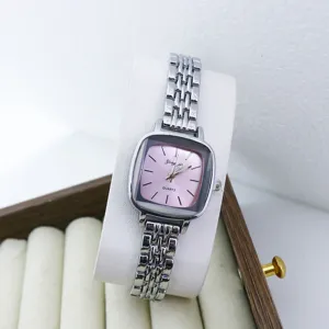 Gros plan sur le détail de la montre quartz à cadran rose carré et bracelet métallique.
