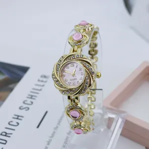 Nahansicht der goldenen floralen Strass-Quarzuhr mit rosa Zifferblatt und Perlenarmband.