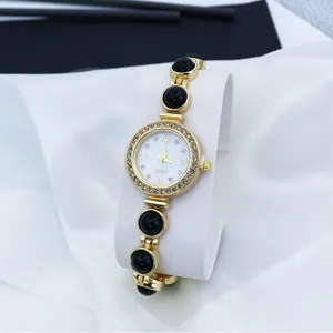 Gedetailleerd anzicht van gouden dames kwarts horloge met strass-stenen en zwarte parels.