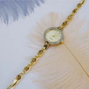 Vista detallada del reloj de mujer dorado con pedrería brillante y cristales marrones.