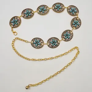 Detalle de cadena de cintura dorada estilo bohemio con eslabones de flores turquesas.