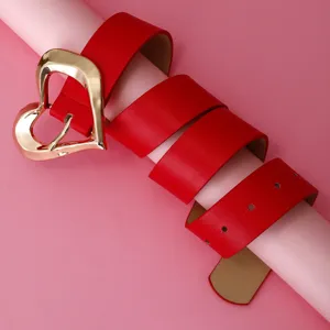 Détail de ceinture en similicuir rouge mettant en valeur la boucle de cœur dorée et sangle.