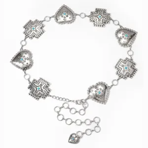 Gros plan détaillé de la chaîne de taille en métal argenté vintage avec croix et cœur turquoise.