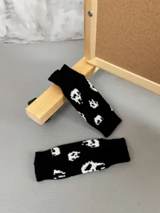 Gros plan détail de gants tricotés noirs demi-doigts avec un motif de crâne blanc.