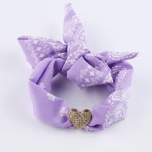 Primo piano dettagliato di un accessorio in tessuto cachemire viola con un ciondolo cuore in cristallo.