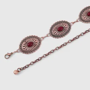Détail de la chaîne de taille métal bohème vintage avec des médaillons gravés et pierre rouge.