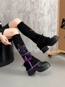 Black knitted leg warmers with purple bow and skull pattern, gothic JK style detail shot.