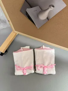 Nahaufnahme von weißen Lolita Strickbeinlingen mit rosa Rippbündchen und Satinbändern.