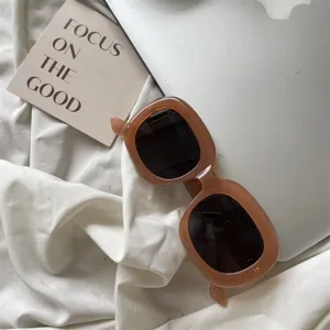 Detailansicht modischer dicker quadratischer Sonnenbrille in Braun auf weißem Stoff.