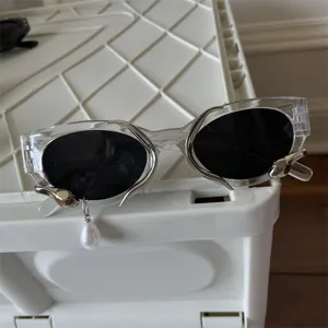 Avantgardistische transparente Sonnenbrille mit Metall-Dekor und Perlenanhänger Detail.
