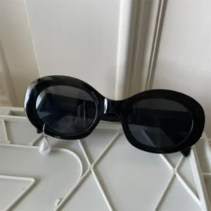 Detailansicht trendiger schwarzer Cat-Eye-Sonnenbrille mit tropfenförmigem Perlenanhänger.