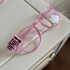 Rosa Y2K transparente Brillenfassung Detail Nahaufnahme mit niedlichem Buchstabenanhänger.