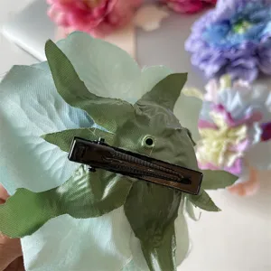 Nahaufnahme des blauen Stoffblumen-Haarclips mit Metall-Krokodilklemme und grüner Blattstruktur.