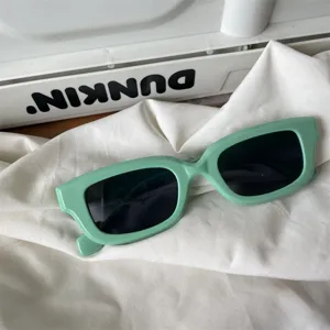 Nahaufnahme der trendigen grünen rechteckigen Sonnenbrille auf weißem Tuch. Modisches Accessoire.