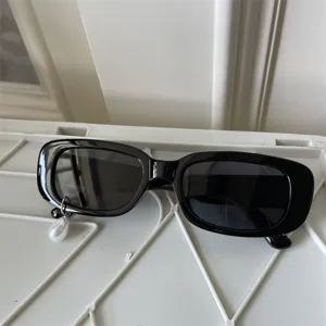 Detailansicht stilvoller schwarzer Rechteck-Sonnenbrille mit Perlenanhänger, trendig.