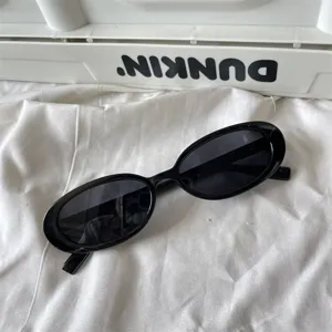 Nahaufnahme einer trendigen schwarzen ovalen Sonnenbrille auf weißem Stoff, minimalistisch.