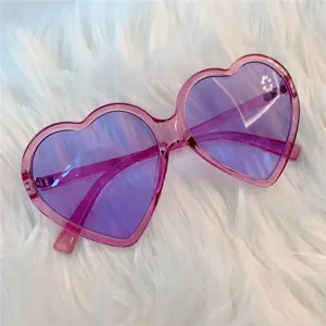 Nahaufnahme von trendigen herzförmigen Sonnenbrillen mit lila Gläsern und rosa Gestell.