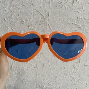 Nahaufnahme von übergroßen herzförmigen Sonnenbrillen mit orangefarbenem Rahmen und blauen Gläsern.