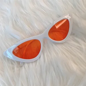 Detailansicht der weißen Cat-Eye-Sonnenbrille mit auffälligen orangen Gläsern auf weichem Pelz.