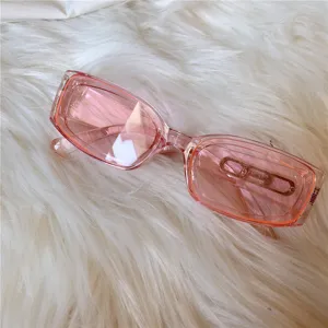 Rosa rechteckige Sonnenbrille Detail mit Metallakzent auf weissem flauschigen Fell Hintergrund.