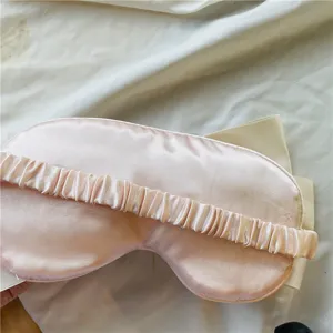 Masque de sommeil en satin rose avec joli nœud et bande élastique pour repos confortable.