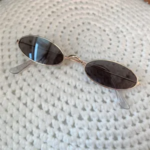 Nahaufnahme von Vintage Mini-Metallsonnenbrille mit ovalen dunklen Gläsern auf Strick.