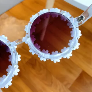 Close-up detail of trendy clear frame sunglasses with cute white daisy flower decorations.
