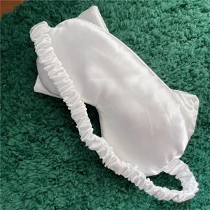 Weisse Satin Schlafmaske Detailansicht mit weichem gerafftem Gummiband fuer bequemen Schlaf.