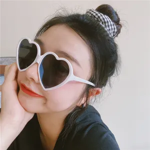 Detailansicht süßer rosafarbener Herz-Sonnenbrille mit weißem Gestell im trendigen Retro-Stil.