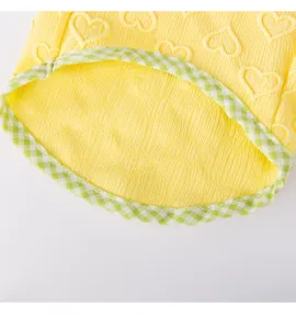 Close-up detail of yellow heart embossed pet apparel with green plaid trim and soft fabric.