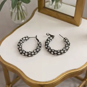 Vue détaillée de créoles tendance en métal noir incrustées de strass transparents scintillants.
