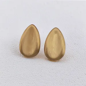 Gros plan sur des boucles d'oreilles pendantes dorées brossées, détail de bijoux élégants.