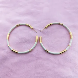 Gros plan de boucles d'oreilles créoles dorées et émail blanc au design bambou unique.