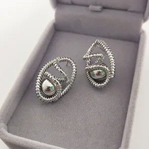 Vue de détail de boucles d'oreilles créoles argentées avec boule métallique.
