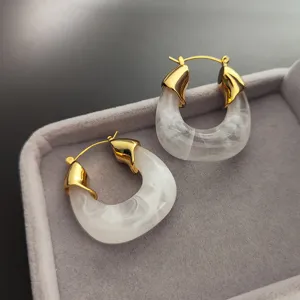 Vue détaillée de boucles d'oreilles créoles épaisses en métal doré et résine blanche.