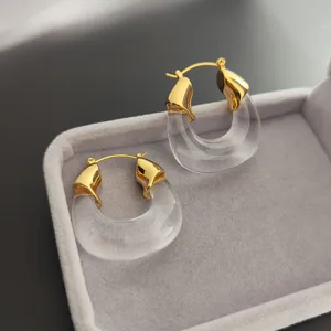 Gros plan détaillé de boucles d'oreilles créoles transparentes en résine et laiton doré.