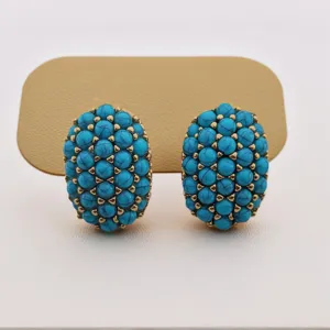 Gros plan de boucles d'oreilles vintage ovales en perles de turquoise avec montures dorées.