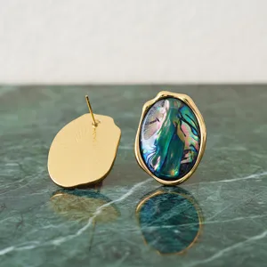 Vue détaillée de boucles d'oreilles ovales irrégulières en abalone et bord doré.