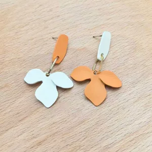 Dettaglio di orecchini pendenti floreali asimmetrici, design chic in metallo e resina.