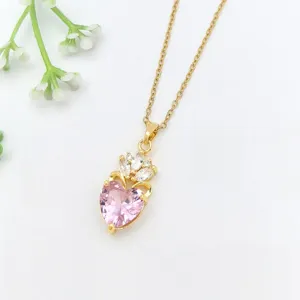 Primo piano dettagliato di una collana dorata con pendente in cristallo a cuore rosa e zirconi.