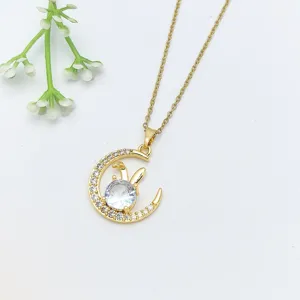 Primo piano dettaglio di una collana in acciaio dorato con ciondolo luna e coniglio in cristallo.