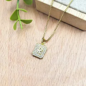Primo piano dettaglio collana con ciondolo lettera R quadrata dorata con zirconi.