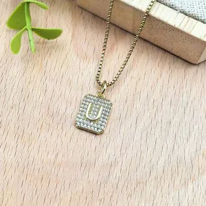 Dettaglio in primo piano della collana con ciondolo a lettera U rettangolare dorata.