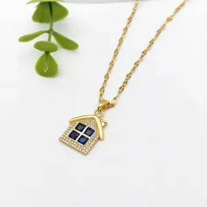 Dettaglio di una collana con ciondolo a forma di casa dorata con zirconi e pietre blu.