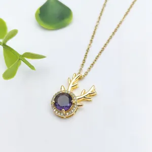 Squisito dettaglio di collana dorata con delicato ciondolo a forma di corno di cervo e gemma viola.
